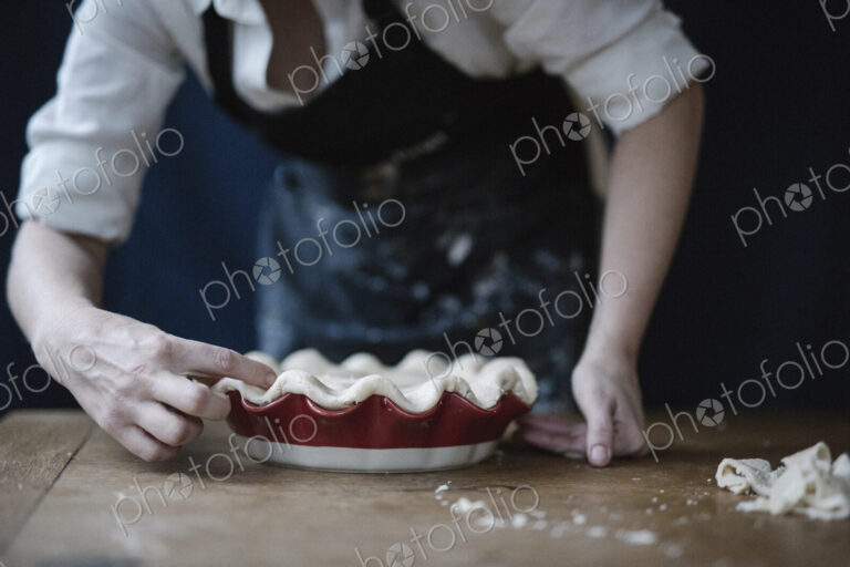 A woman in a kitchen decorating the pastry top of a home made pie.