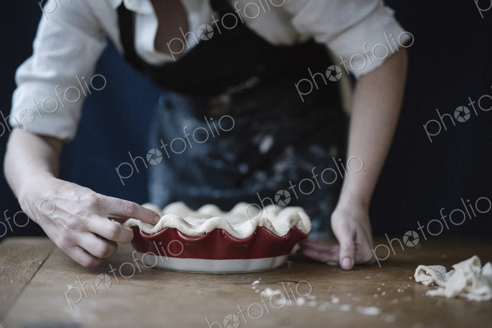 A woman in a kitchen decorating the pastry top of a home made pie.