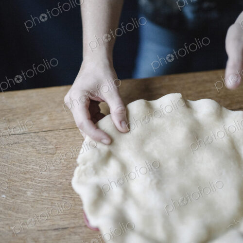 A woman in a kitchen decorating the pastry top of a home made pie. A woman in a kitchen decorating the pastry top of a home made pie.