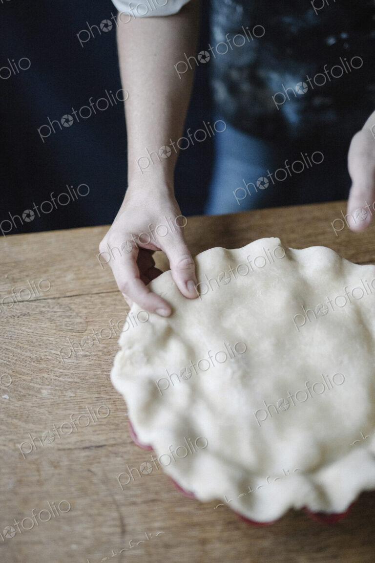 A woman in a kitchen decorating the pastry top of a home made pie.