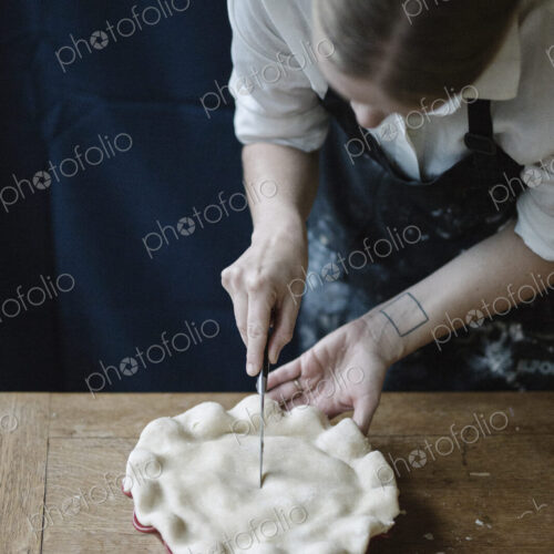 A woman in a kitchen decorating the pastry top of a home made pie. A woman in a kitchen decorating the pastry top of a home made pie.