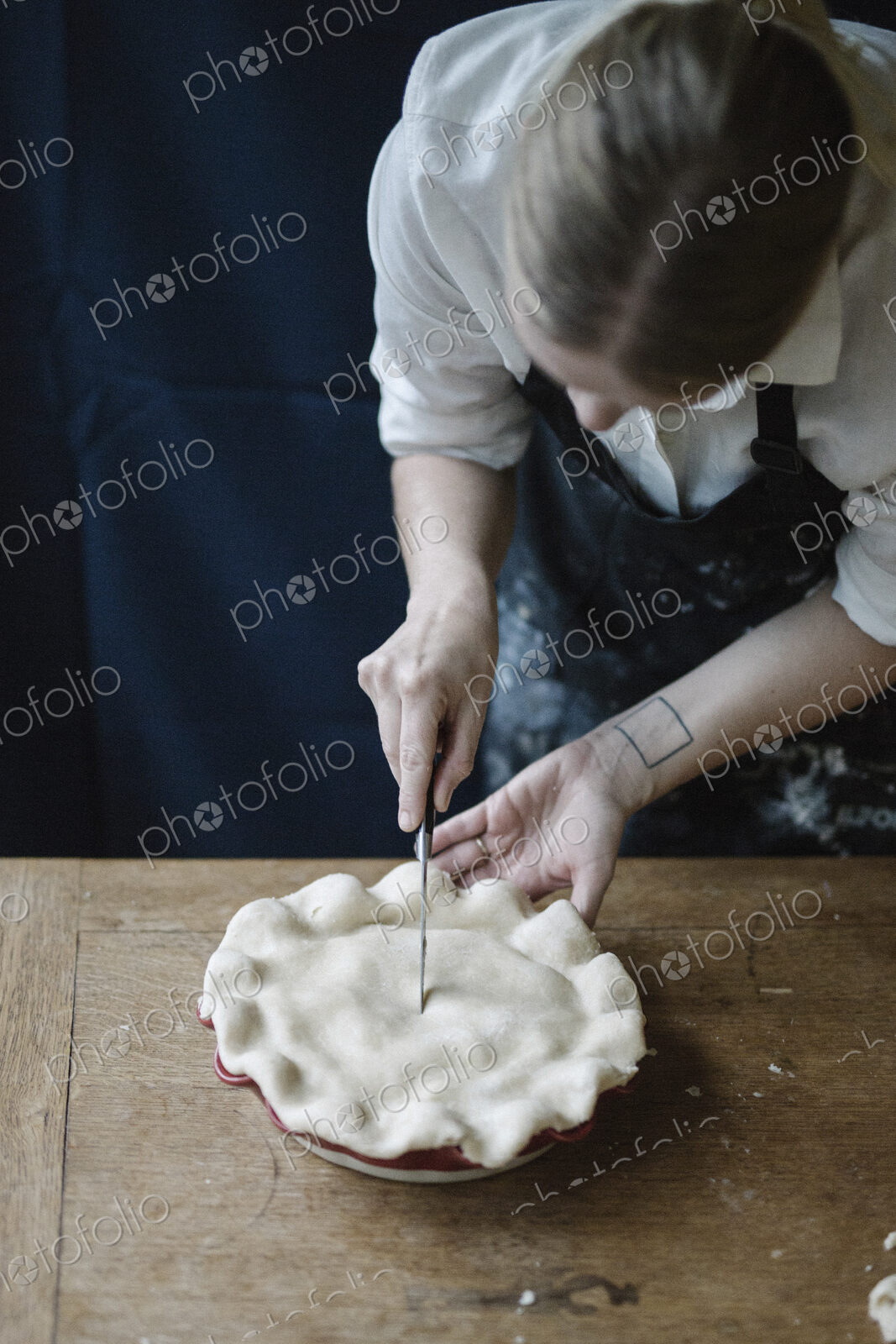 A woman in a kitchen decorating the pastry top of a home made pie.