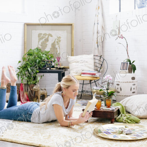 A woman in a light airy apartment relaxing, lying on the floor reading a book. A woman in a light airy apartment relaxing, lying on the floor reading a book.