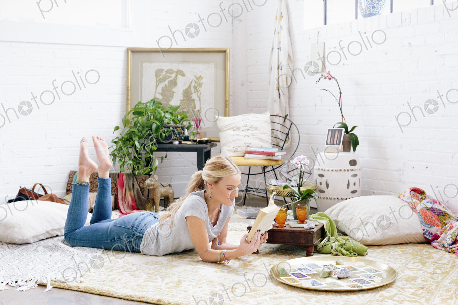 A woman in a light airy apartment relaxing, lying on the floor reading a book.