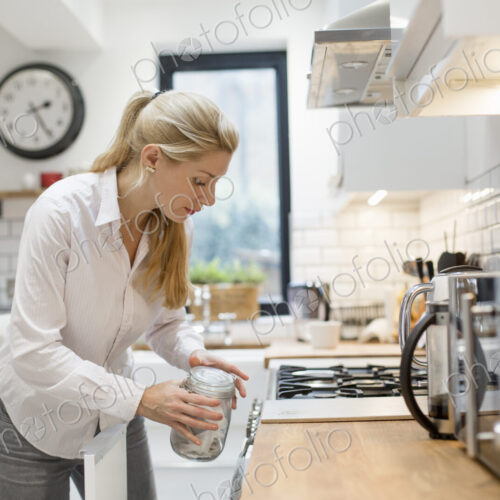 A woman in a modern kitchen holding a jar with a lid. A woman in a modern kitchen holding a jar with a lid.