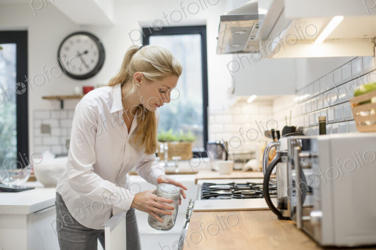 A woman in a modern kitchen holding a jar with a lid.