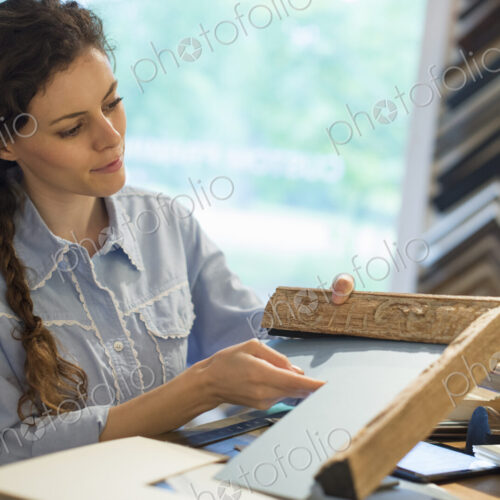 A woman in a picture framer's workshop, choosing frames and cardboard mounts.…