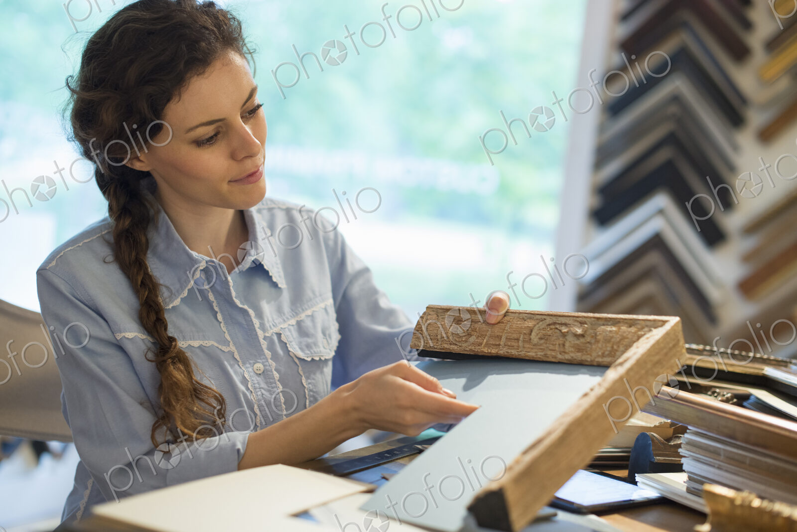 A woman in a picture framer’s workshop, choosing frames and cardboard mounts.…