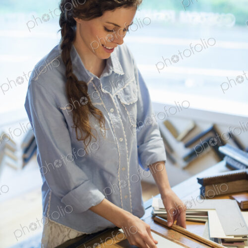 A woman in a picture framer's workshop, choosing frames and cardboard mounts.…