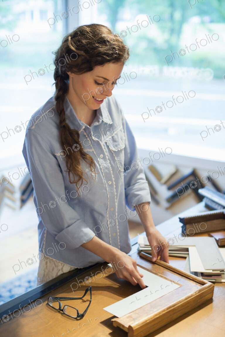 A woman in a picture framer's workshop, choosing frames and cardboard mounts.…
