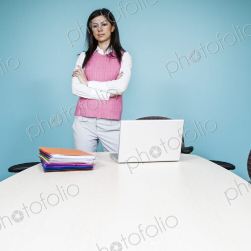 A woman in a pink top at a conference room table with a blue painted wall. A woman in a pink top at a conference room table with a blue painted wall.