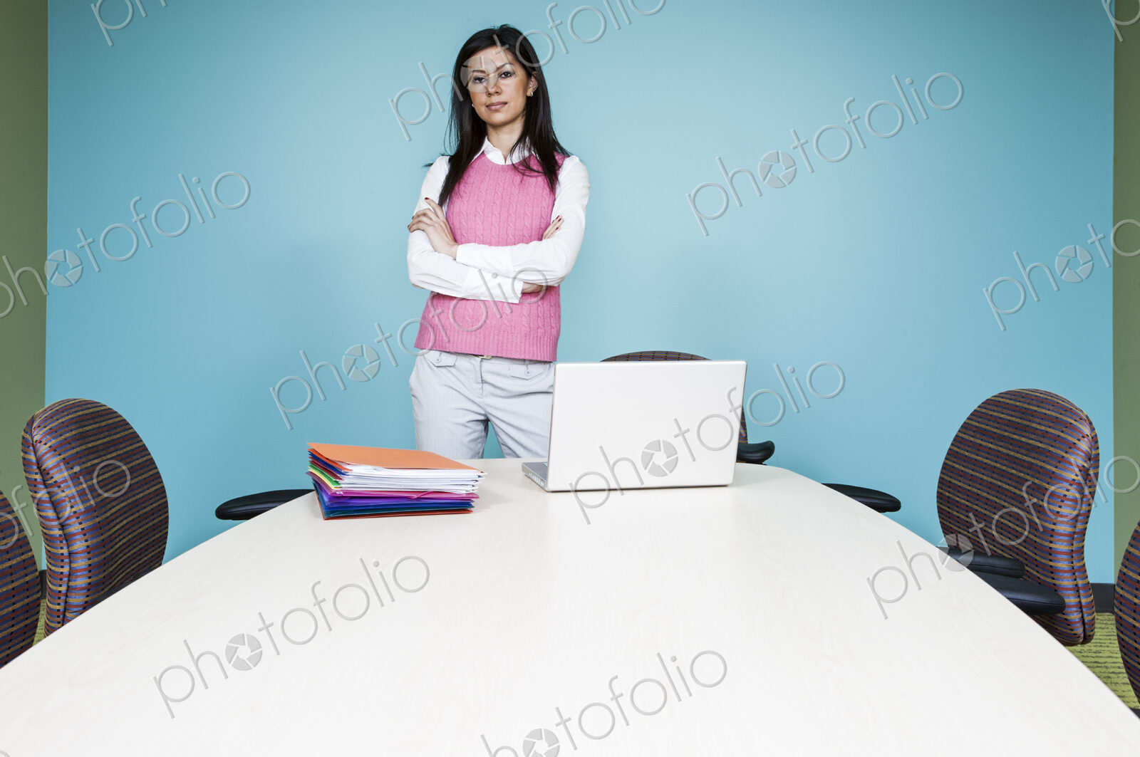 A woman in a pink top at a conference room table with a blue painted wall.