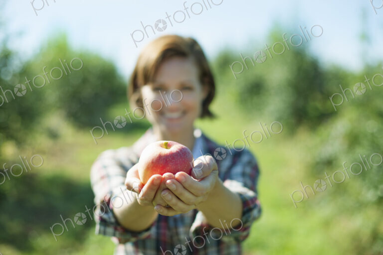 A woman in a plaid shirt holding a freshly picked apple in her cupped hands in the…