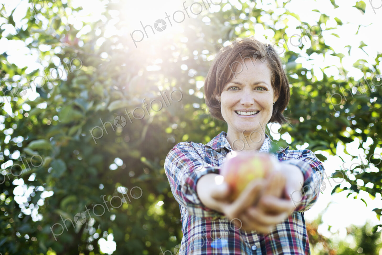 A woman in a plaid shirt holding a freshly picked apple in her two hands, in the…