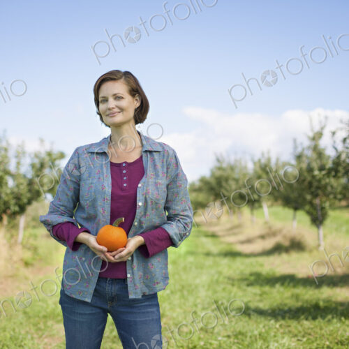 A woman in a plaid shirt holding an orange pumpkin or squash in her cupped hands, at… A woman in a plaid shirt holding an orange pumpkin or squash in her cupped hands, at…
