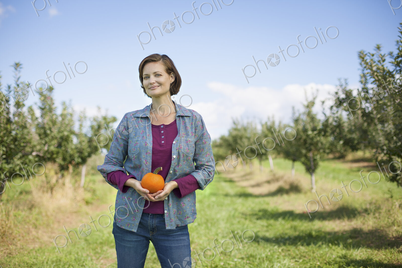 A woman in a plaid shirt holding an orange pumpkin or squash in her cupped hands, at…