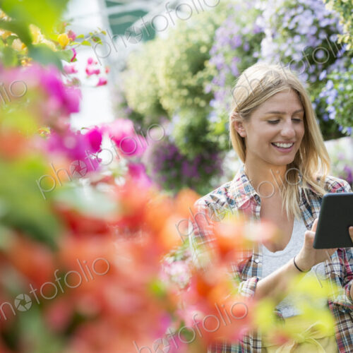 A woman in a plant nursery surrounded by flowering plants and green foliage. A woman in a plant nursery surrounded by flowering plants and green foliage.