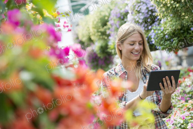 A woman in a plant nursery surrounded by flowering plants and green foliage.