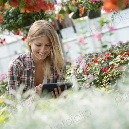 A woman in a plant nursery surrounded by flowering plants and green foliage. A woman in a plant nursery surrounded by flowering plants and green foliage.