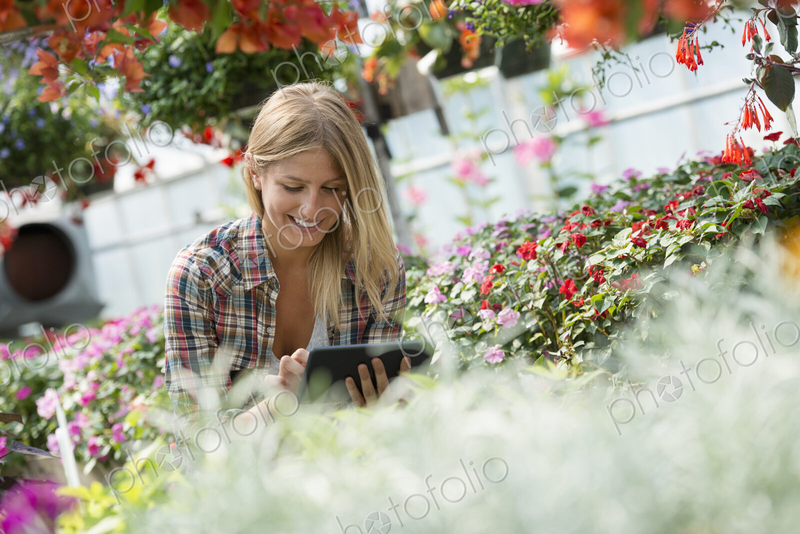 A woman in a plant nursery surrounded by flowering plants and green foliage.