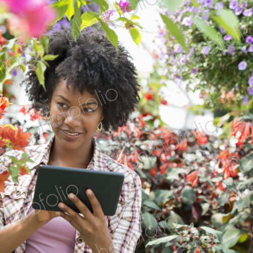 A woman in a plant nursery surrounded by flowering plants and green foliage. A woman in a plant nursery surrounded by flowering plants and green foliage.