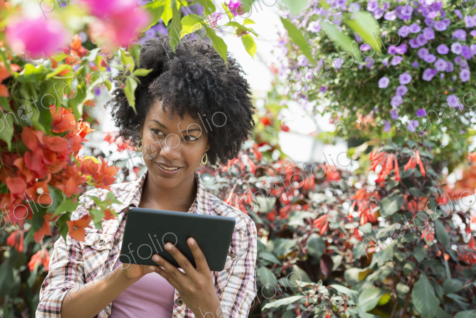 A woman in a plant nursery surrounded by flowering plants and green foliage.