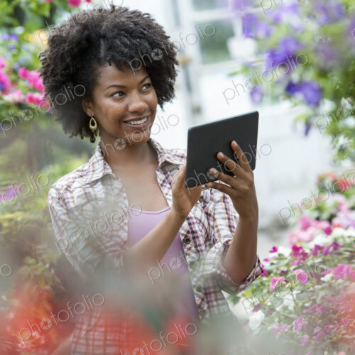 A woman in a plant nursery surrounded by flowering plants and green foliage. A woman in a plant nursery surrounded by flowering plants and green foliage.