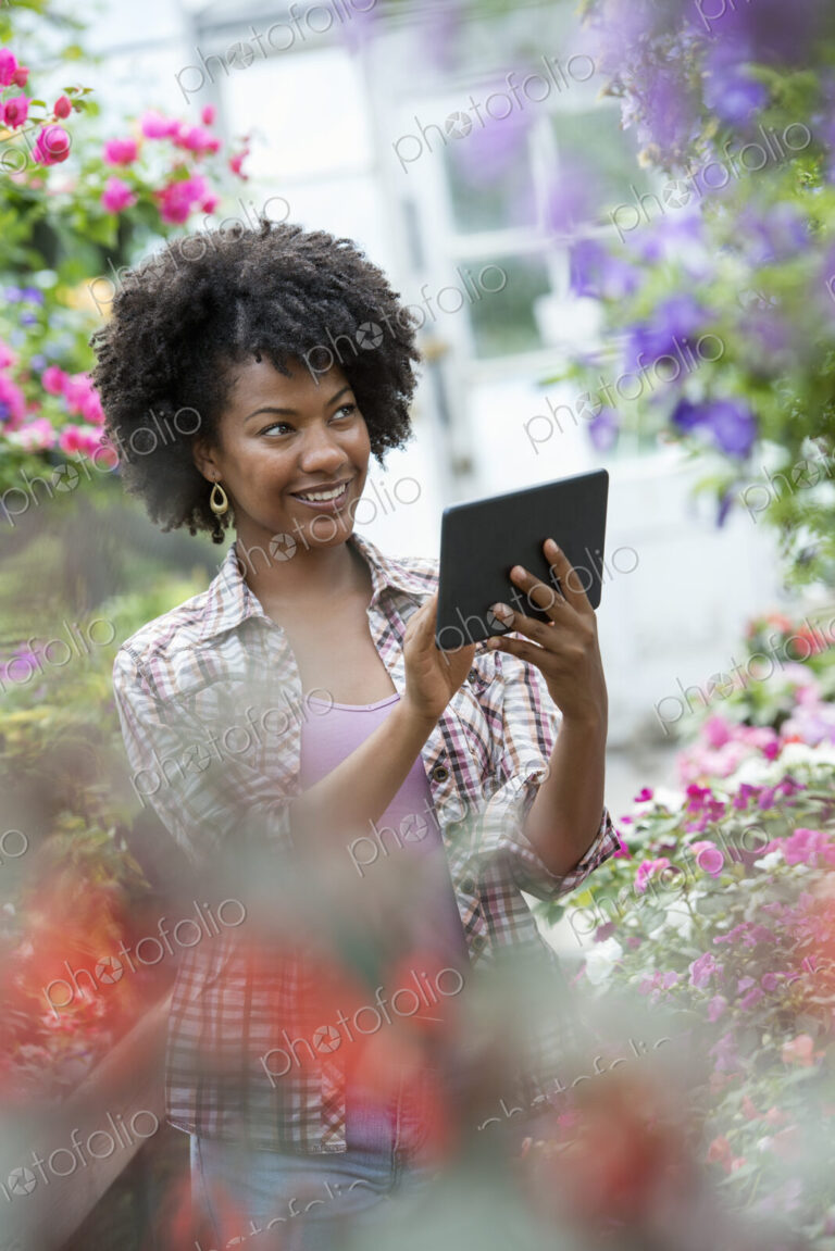 A woman in a plant nursery surrounded by flowering plants and green foliage.