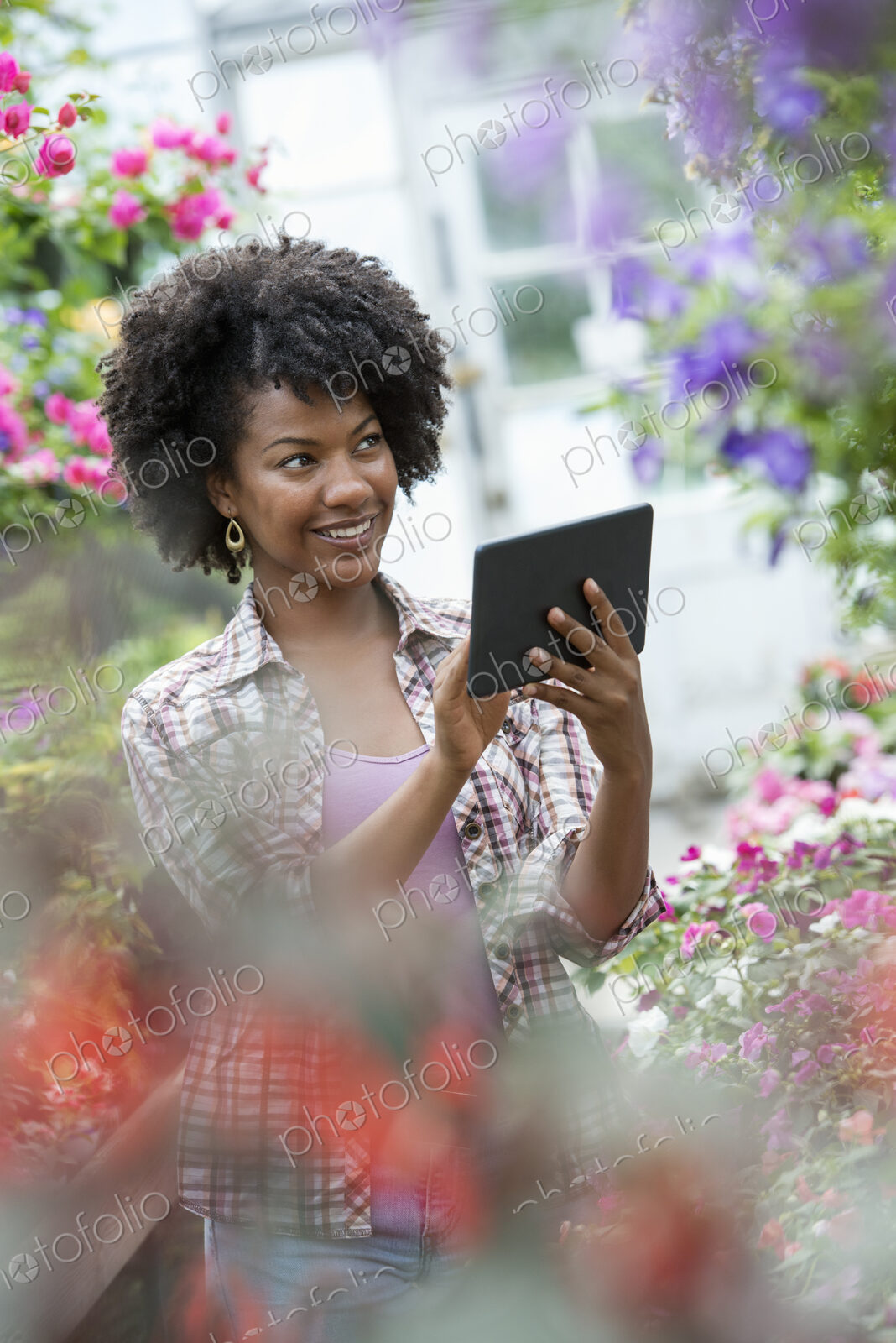 A woman in a plant nursery surrounded by flowering plants and green foliage.