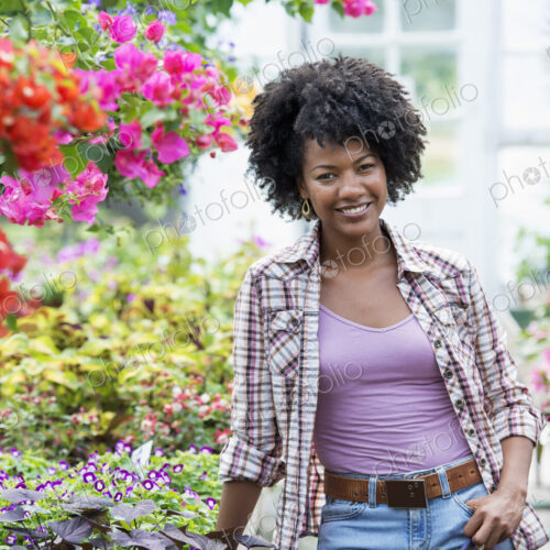 A woman in a plant nursery surrounded by flowering plants and green foliage. A woman in a plant nursery surrounded by flowering plants and green foliage.