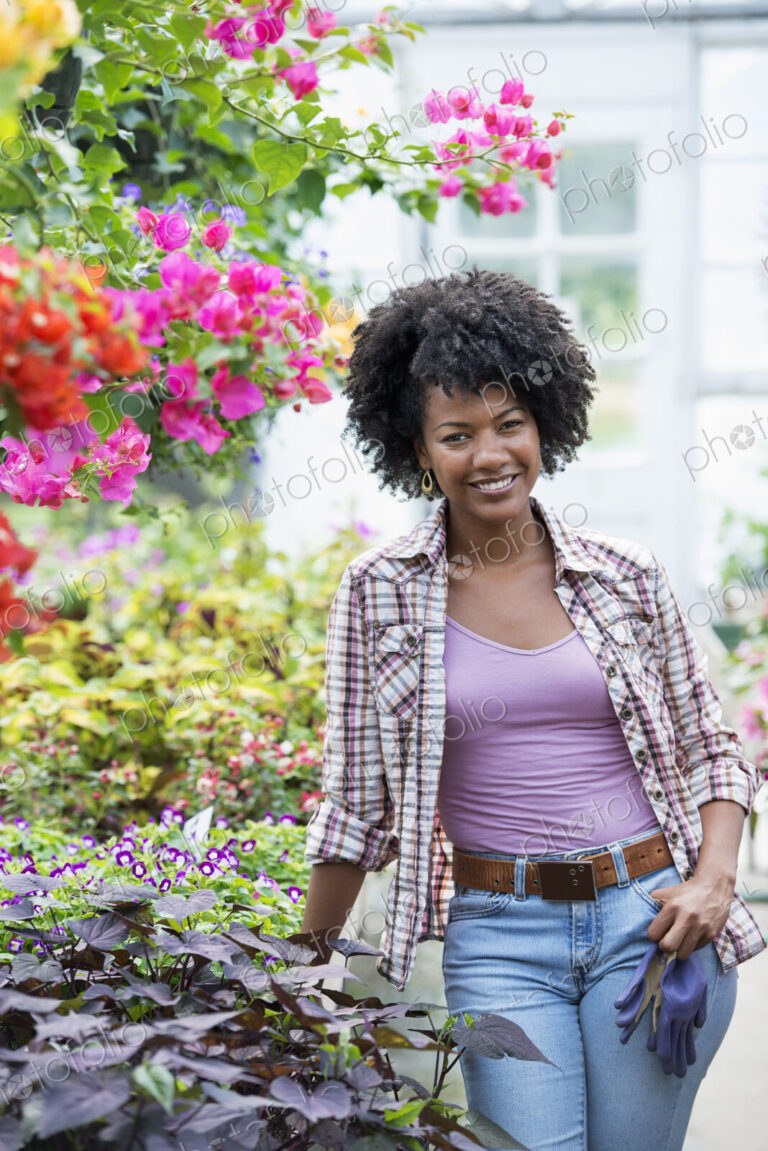 A woman in a plant nursery surrounded by flowering plants and green foliage.