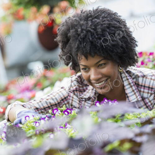A woman in a plant nursery surrounded by flowering plants and green foliage. A woman in a plant nursery surrounded by flowering plants and green foliage.