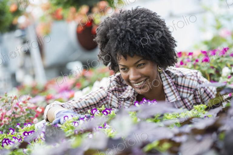 A woman in a plant nursery surrounded by flowering plants and green foliage.