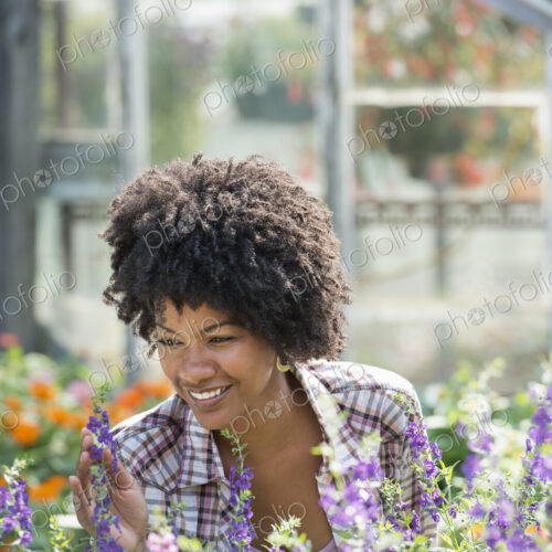 A woman in a plant nursery surrounded by flowering plants and green foliage. A woman in a plant nursery surrounded by flowering plants and green foliage.