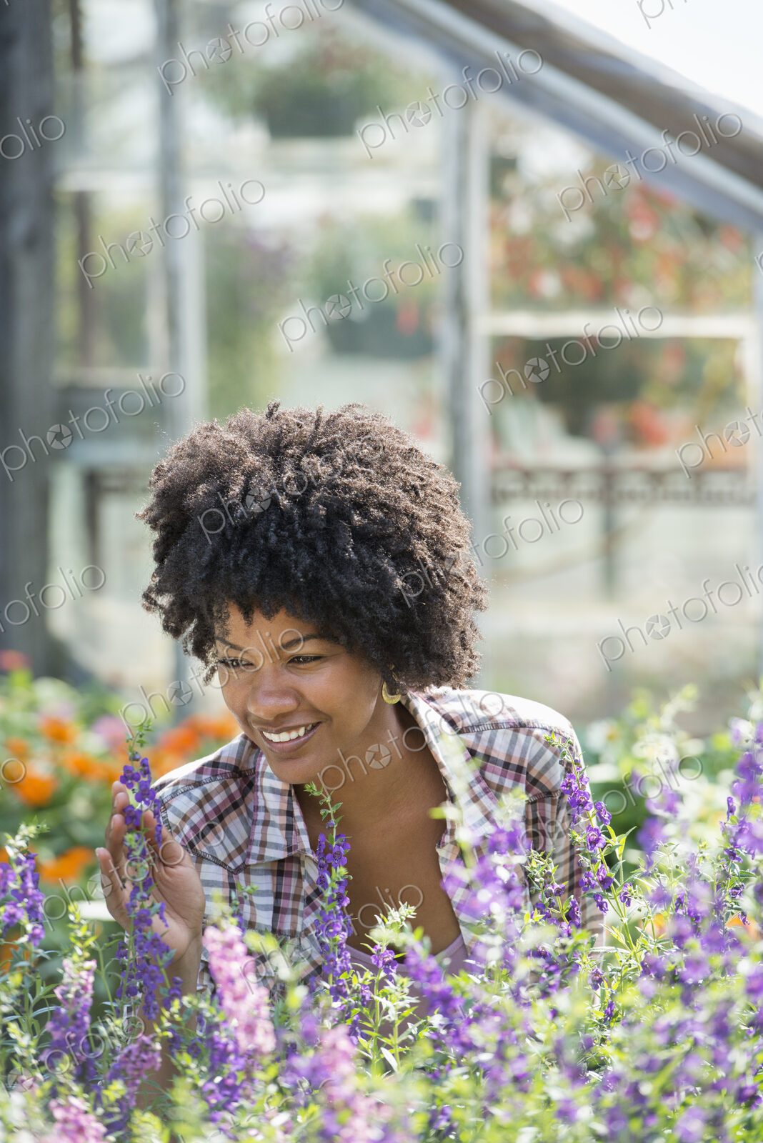 A woman in a plant nursery surrounded by flowering plants and green foliage.