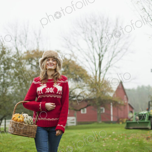 A woman in a red knitted jumper holding a basket of vegetables, gourds and squashes.… A woman in a red knitted jumper holding a basket of vegetables, gourds and squashes.…