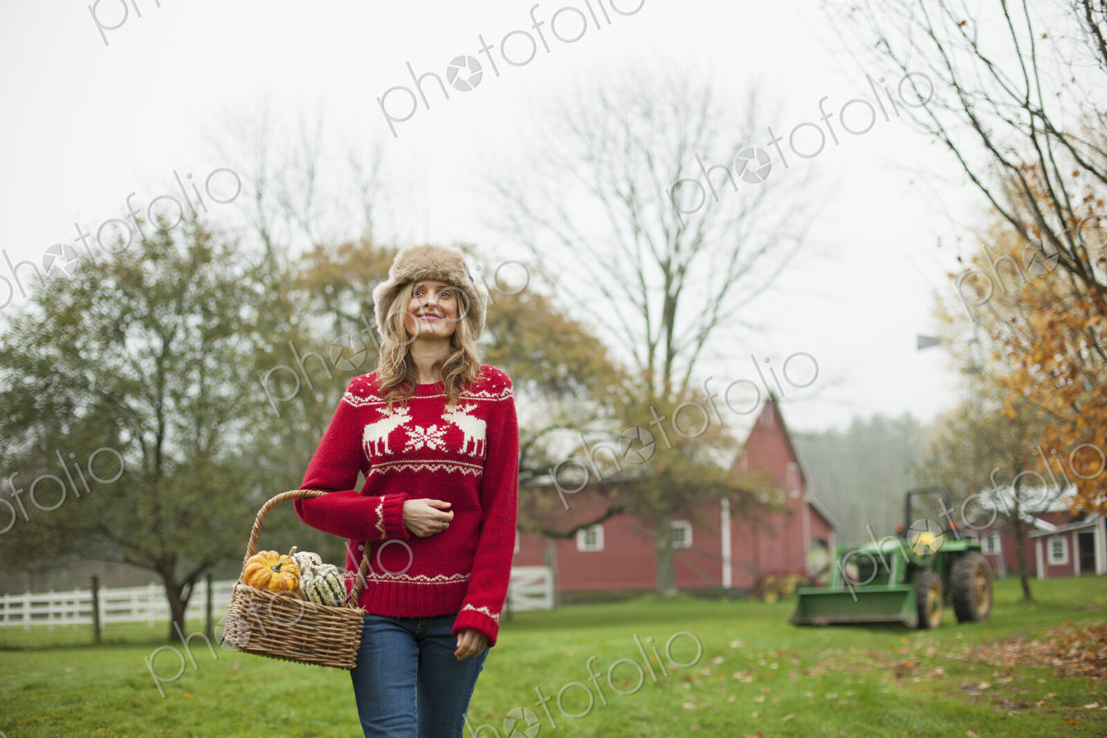 A woman in a red knitted jumper holding a basket of vegetables, gourds and squashes.…