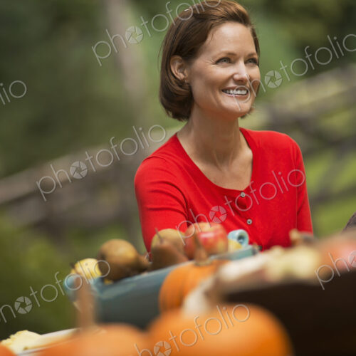 A woman in a red shirt, at a harvest table outdoors. A woman in a red shirt, at a harvest table outdoors.