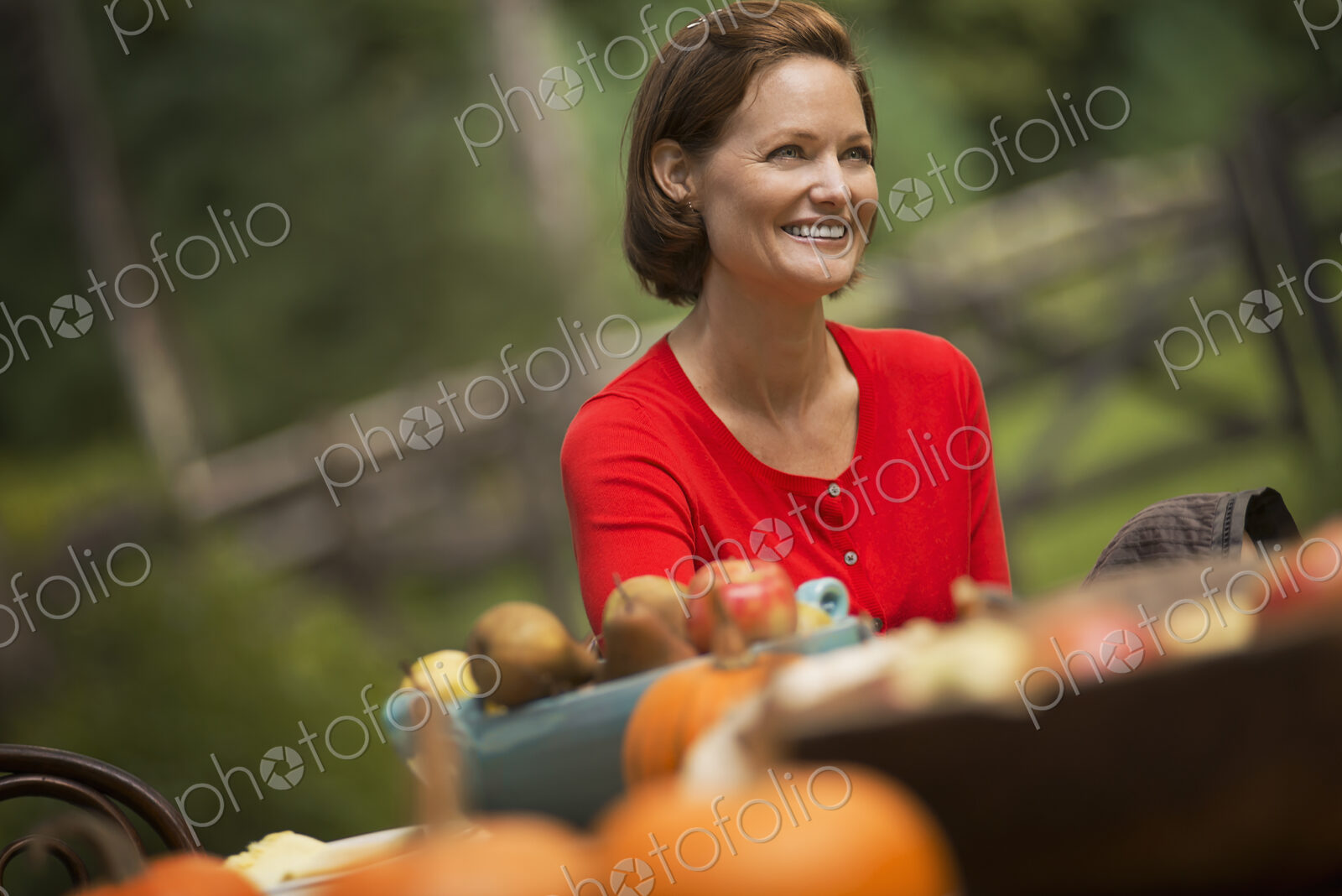 A woman in a red shirt, at a harvest table outdoors.