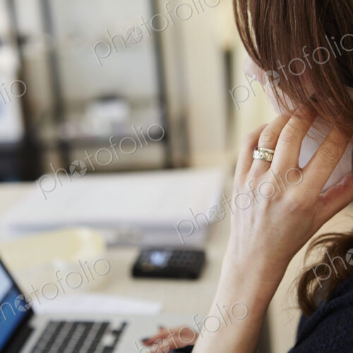A woman in a shop on her laptop, making a phone call.