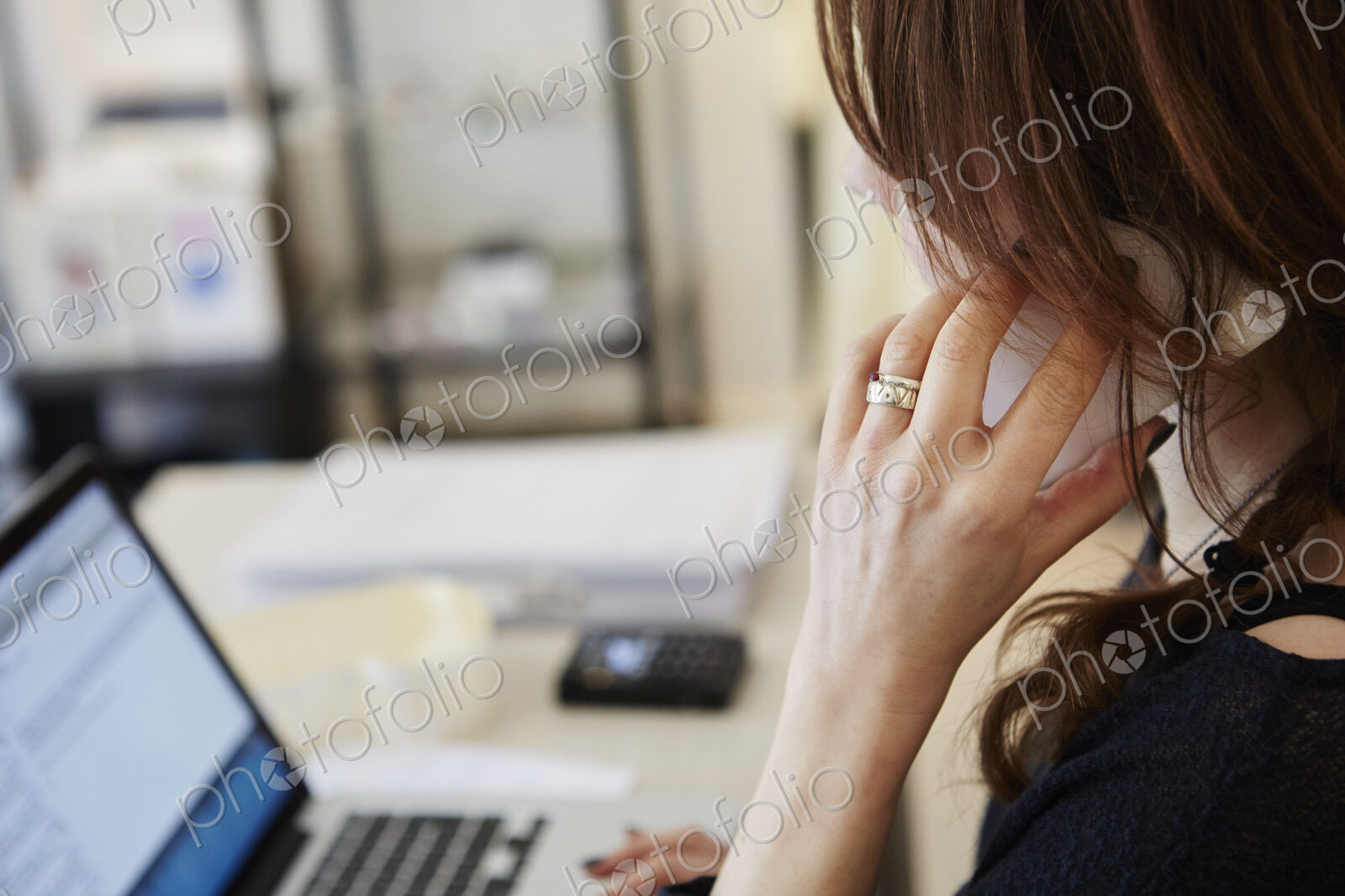 A woman in a shop on her laptop, making a phone call.