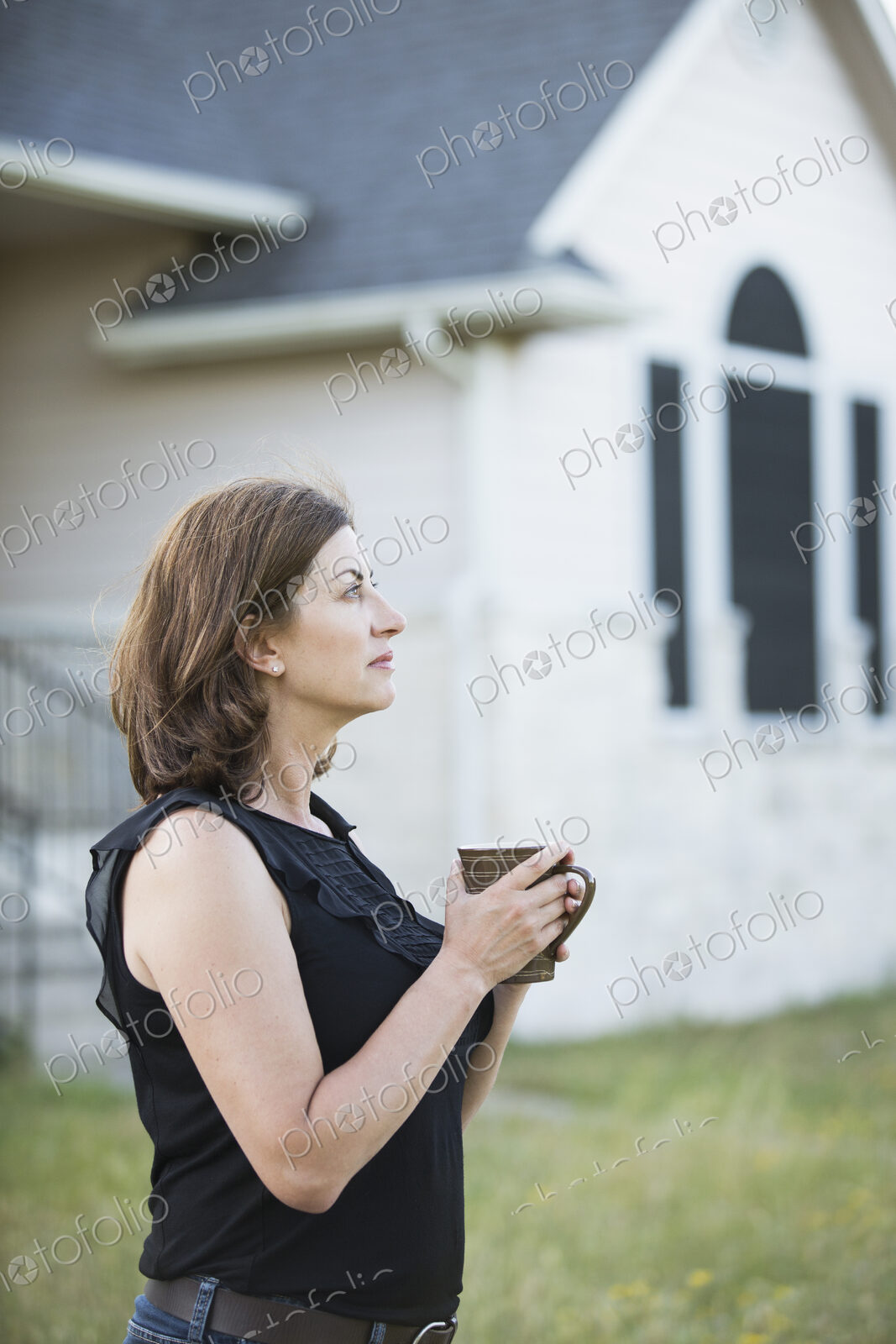 A woman in a sleeveless shirt holding a cup in her hands, standing outside a country…