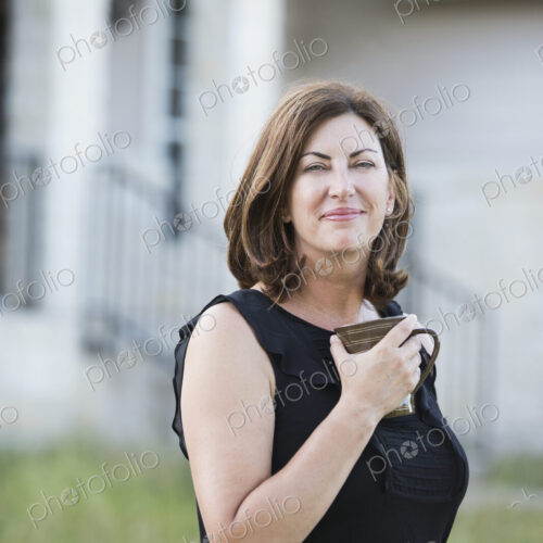 A woman in a sleeveless shirt holding a cup in her hands, standing outside a country… A woman in a sleeveless shirt holding a cup in her hands, standing outside a country…