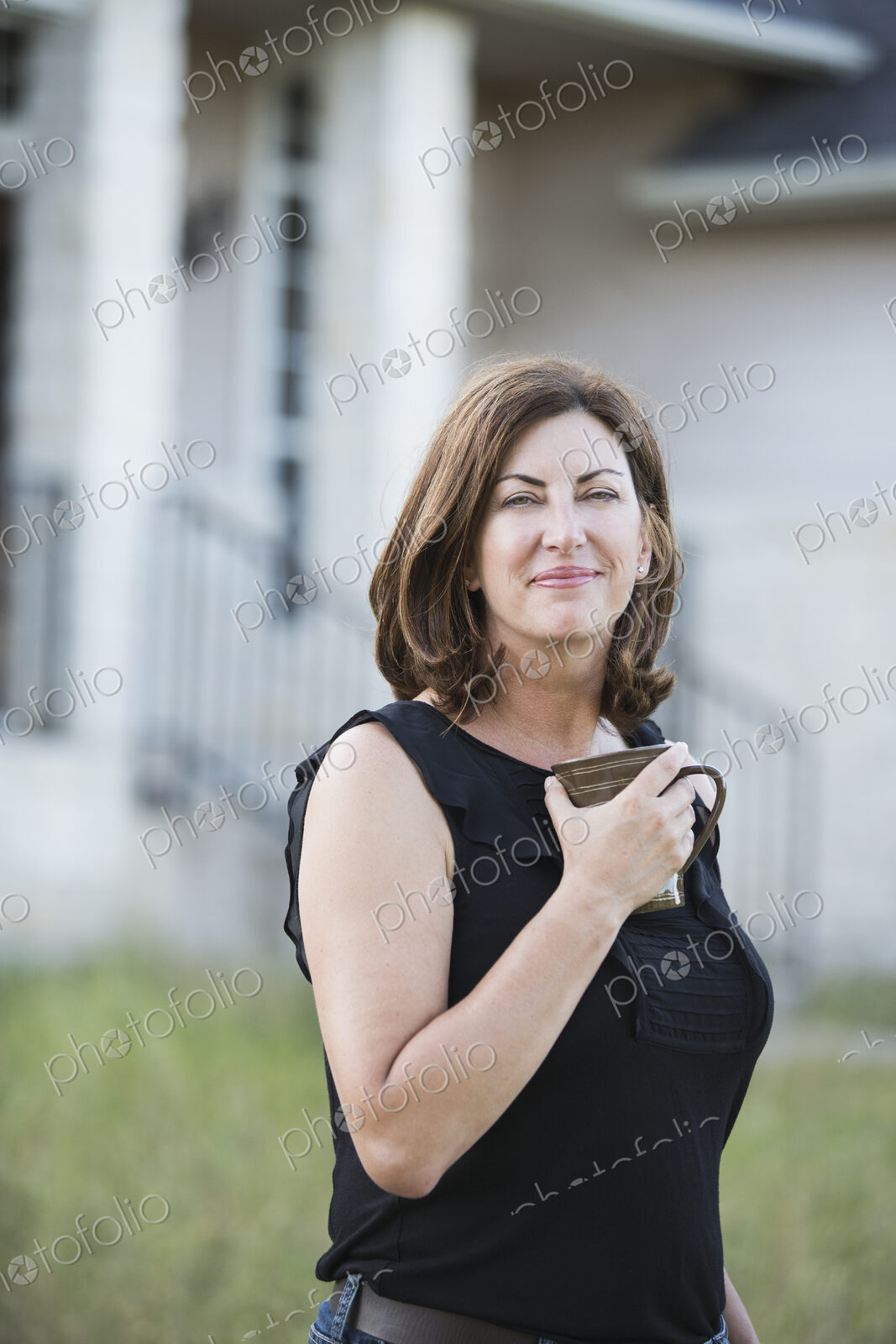 A woman in a sleeveless shirt holding a cup in her hands, standing outside a country…