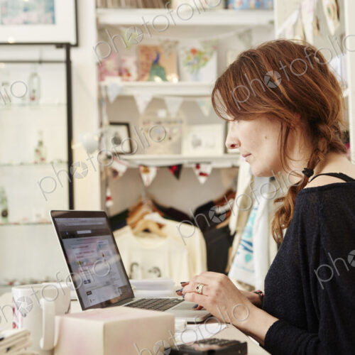 A woman in a small crafts supplier and gift shop, using a laptop, working,