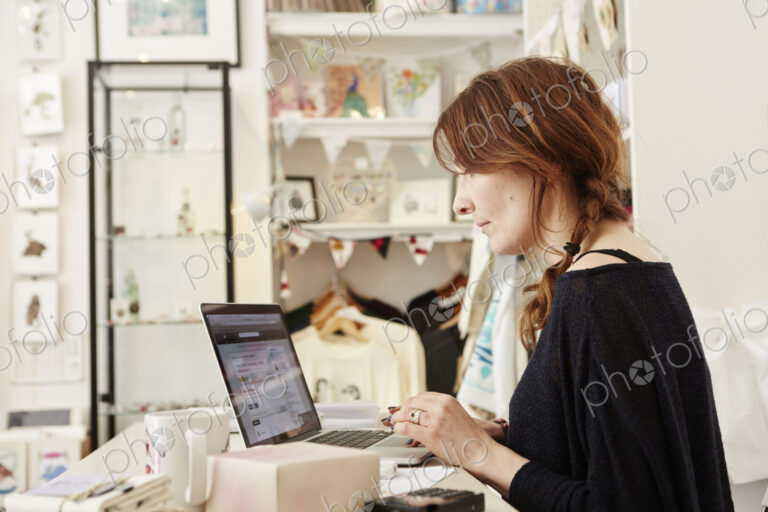 A woman in a small crafts supplier and gift shop, using a laptop, working,