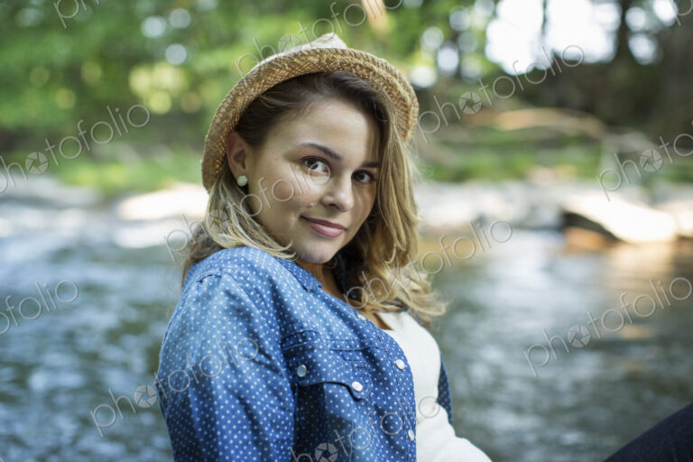 A woman in a straw hat on a river bank.