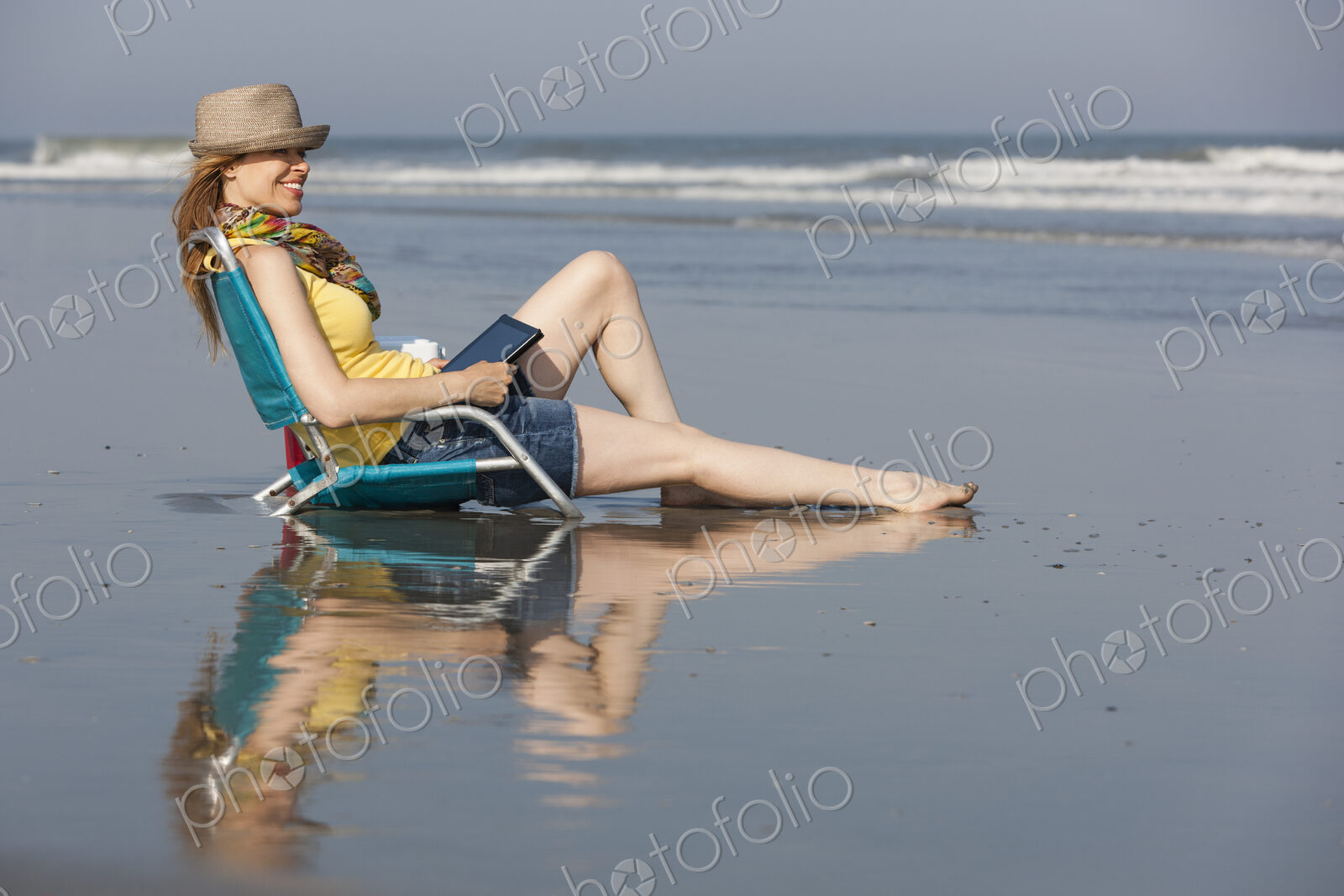 A woman in a sunhat and scarf on the beach on the New Jersey Shore, sitting holding a…