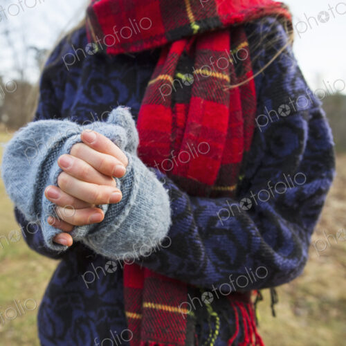 A woman in a tartan scarf and knitted woollen mitts, keeping her hands warm in cold… A woman in a tartan scarf and knitted woollen mitts, keeping her hands warm in cold…