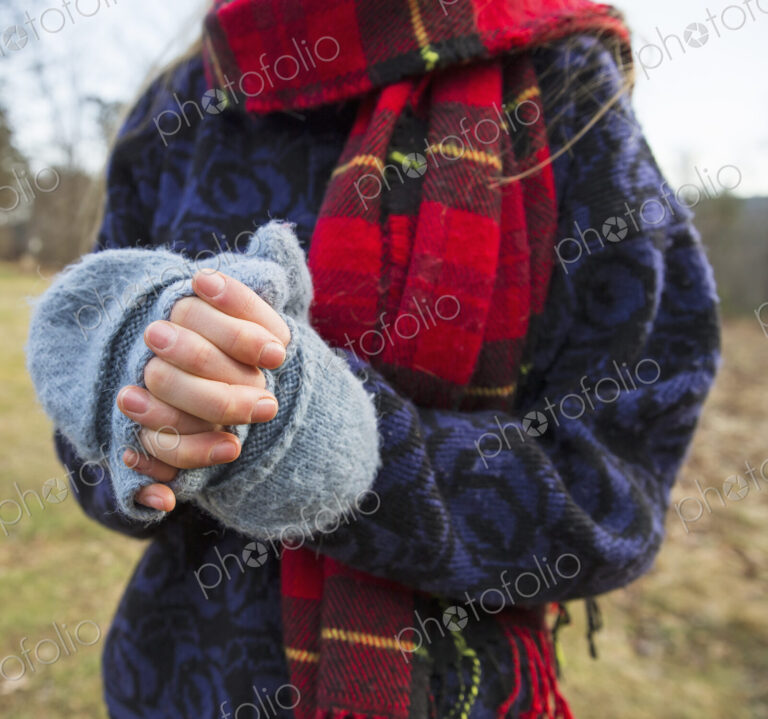 A woman in a tartan scarf and knitted woollen mitts, keeping her hands warm in cold…